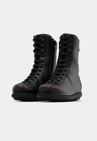 Černé kožené boty s vysokým lýtkem, vybavené šněrováním vpředu a bočním zipem. Silná gumová podešev s texturovaným vzorkem a zaoblenou špičkou.