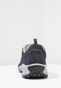 Tummansinisestä denimi-kankaasta valmistettu kangaskenkä, jossa oranssit ompeleet, harmaa kumipohja, pyöristetty muotoilu ja helppoa pukemista varten takana oleva vetolenkki.