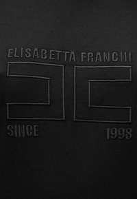 Μαύρο ένδυμα με υφή μαύρης κεντητικής. Το κείμενο περιλαμβάνει τις λέξεις "ELISABETTA FRANCHI", "DC" και "ΑΠΌ ΤΟ 1998" με στιλιζαρισμένη γραμματοσειρά.