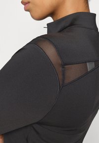 Top sportiv negru cu guler înalt, panouri din plasă pe umeri și cusături fără sudură pentru un design elegant și ajustat.