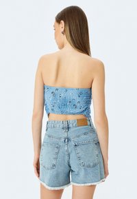 Blauw, gesmokte, strapless crop top met zwarte print, gecombineerd met lichte denim high-waisted shorts met rafelige randen en een bruin label.