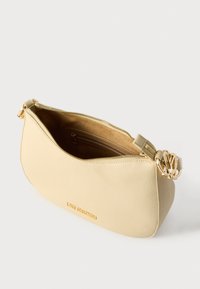 Μπεζ τσάντα ώμου από υφή δέρματος με καμπυλωτό σχήμα, χρυσούς μεταλλικούς εξαρτήματα και κλείσιμο με φερμουάρ. Διαθέτει εσωτερική θήκη για οργάνωση.