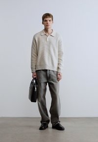 Γκρι ανοιχτόχρωμο, υφασμάτινο πουλόβερ με γιακά, φορεμένο με άνετο γκρι τζιν παντελόνι. Μαύρη τσάντα κρατημένη με το ένα χέρι, μαύρα παπούτσια ολοκληρώνουν το σύνολο.