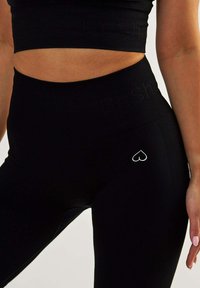 Black ribbed leggings with a high waist, featuring a small heart logo in white on the side. Made from stretchy, form-fitting material.