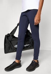 Marineblauwe sportbroek in een slanke pasvorm, van een katoenen mengsel, met ribgebreide boorden, gecombineerd met een zwarte sporttas met witte branding en zwarte mesh-accenten.