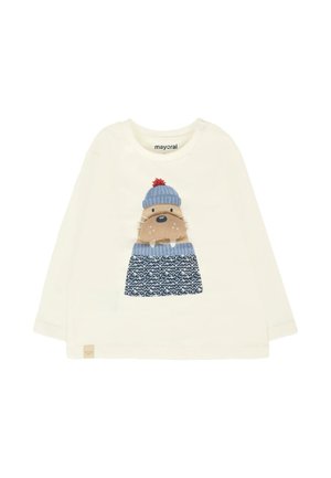 Maglietta a maniche lunghe color crema con un walruss dei cartoni animati che indossa un cappello blu con pom-pon rosso e una sciarpa blu a fantasia su uno sfondo di maglia blu.