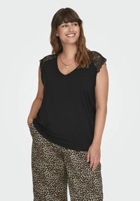 Top in cotone nero con bordi in pizzo sulle spalle e scollatura a V, abbinato a pantaloni a vita larga con stampa leopardata.