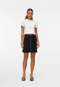 Witte cropped t-shirt in combinatie met een zwarte denim rok met een rits aan de voorkant. Het materiaal lijkt glad; de rok heeft een lichte flare.