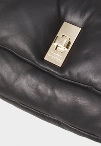 Borsa a mano in pelle nera con un importante fermo dorato con marchio inciso, texture liscia e elementi di design arricciati.