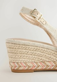 Bézs színű szövött ék szandál bokapánttal, arany csattal és fonott juta talppal, rózsaszín és fehér cikk-cakk mintákkal díszítve.