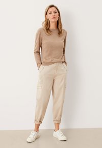 Maglione lavorato a maglia beige con scollo rotondo abbinato a pantaloni cargo beige chiaro con tasche, risvolti e sneakers bianche.
