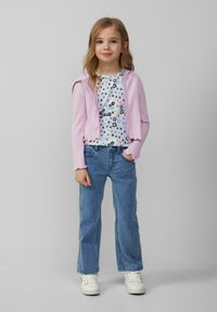 Hellblauer, gerippter Reißverschluss-Cardigan über einem floral gemusterten weißen T-Shirt, kombiniert mit blauen geraden Jeans und weißen Turnschuhen.