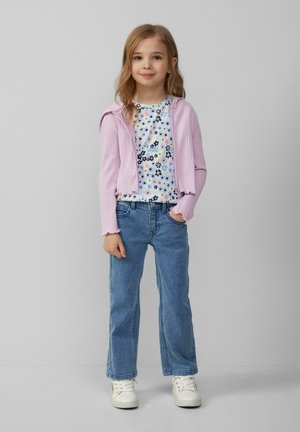 Lichtpaarse ribgebreide zip-up cardigan over een wit T-shirt met bloemenpatroon, gecombineerd met blauwe straight-leg jeans en witte sneakers.