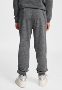 Graue Jogginghosen mit lockerer Passform, strukturiertem Stoff, elastischem Bund und Bündchen, kombiniert mit weißen Sneakern mit silbernen Akzenten.