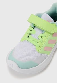 Baskets de sport vertes et blanches avec une tige en mesh, une sangle réglable et une semelle en caoutchouc. Accents notables en rose et bleu clair.