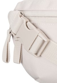 Svetlá nylonová taška s textúrovaným povrchom, vybavená plastovým prackom a popruhom, zdôrazňujúca funkčné dizajnové prvky.