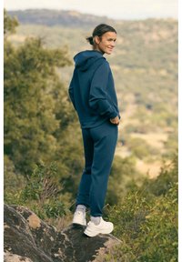 Sudadera de color azul oscuro y pantalones jogger a juego, confeccionados en una tela suave, con un corte relajado, bolsillos y combinados con zapatillas blancas.