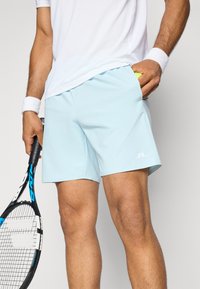 Shorts atléticos de cor azul clara feitos de tecido sintético, com um logótipo, bolsos laterais e um cós elástico, acompanhados de uma camisa branca e uma raquete de ténis.