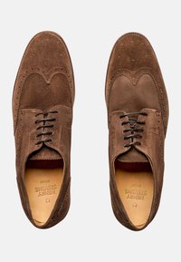 Braune Wildleder-Brogueschuhe mit perforierten Details, Schnürverschluss und glatter Innenausstattung. Flache Laufsohle. Klassisches Wingtip-Design.