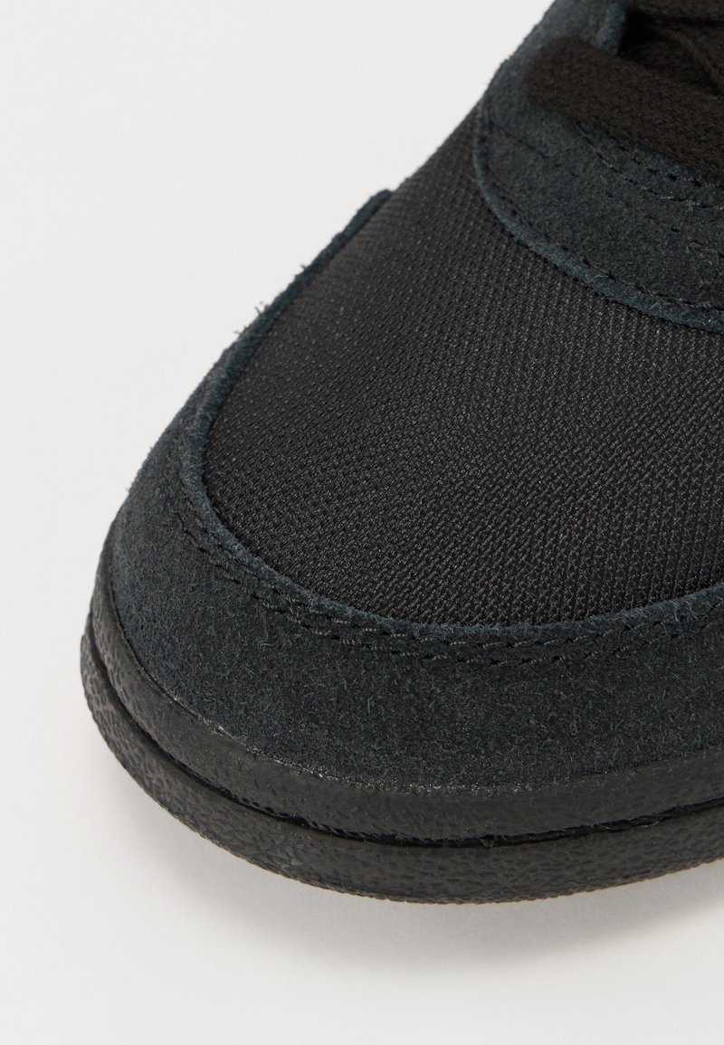 Czarne sneakersy z połączeniem gładkiego materiału tekstylnego i zamszu. Posiadają zaokrąglony czubek, fakturowaną powierzchnię i gumową podeszwę.