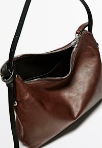 Borsa a mano in pelle marrone con forma curva, manico nero e zipper argentato. Interno in tessuto nero. Nessuna tasca esterna visibile.