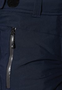 Marinblå byxor med en mjuk textur, med en sidoficka med dragkedja som har grå detaljer och en rund svart kardborreknäppning.