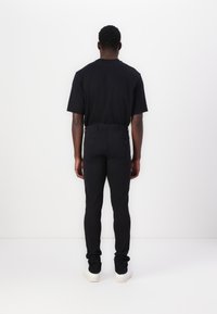 Black short-sleeve shirt paired with fitted black pants and white sneakers, viewed from the back against a plain white background.