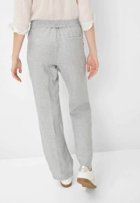 Lichtgrijze linnen broek met een elastische tailleband, voorzien van een achterzak en een relaxte, rechte pasvorm. Gedragen met witte schoenen.