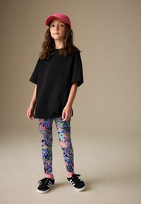 Tricou negru supradimensionat asortat cu colanți colorați, cu modele și pete roz, albastre și verzi. Adidași negri cu accente roz.