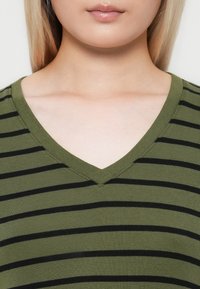 Close-up of neck and lower face of person wearing green and black striped V-neck shirt.