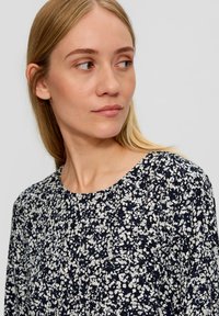 Marineblaue Bluse mit floralen Muster, runden Halsausschnitt, leichtem Stoff und einem verstreuten weißen Blumenmuster.