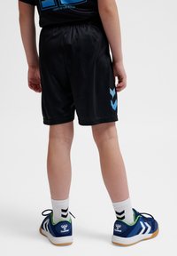Zwarte sportshorts met een elastische tailleband, gekenmerkt door een blauw chevronontwerp aan de zijkant; gecombineerd met blauwe sportschoenen en witte sokken.