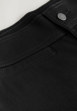 Primo piano di un tessuto di denim nero caratterizzato da una texture liscia, cuciture a contrasto e un dettaglio in metallo sul cinturino.