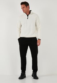 Hvid fleece trøje med lynlås-krave, parret med sorte tapered bukser og sorte ankelstøvler, der har en afslappet pasform og tekstureret stof.