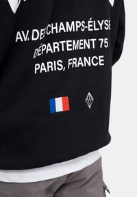 Felpa nera con testo bianco e una toppa della bandiera francese. Logo geometrico notevole ricamato accanto alla bandiera. Vestibilità casual.