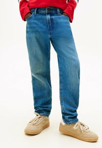Jeans de denim azul con un corte relajado, que presentan un lavado desgastado y un diseño de cinco bolsillos, combinados con zapatillas beiges.