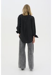 Black long-sleeve shirt with a loose fit, featuring a back pleat. Paired with light gray wide-leg denim pants and visible stitching details.