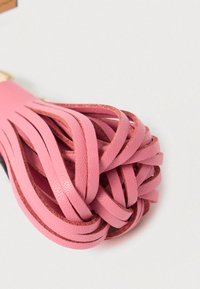 Rozā ādas bārkstis ar vairākām faktūrām, cieši savāktas augšdaļā un šaurākas apakšā, parādot gludu virsmu.