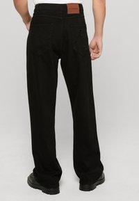 Mustad laiad püksid, mis on valmistatud pehmest kangast ja millel on nahast vöökoht. Omab kahte tagumist taskut, millel on toon-toonis tikandiga logo detail.