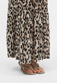Φούστα με λευκές σε στρώσεις και σανδάλια μπεζ χρώματος σε λευκό φόντο, δείχνει τα κάτω πόδια και τα πόδια.