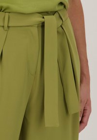 Groene broek met een zelfstrikriem in de taille, gemaakt van een gladde, gestructureerde stof en met zijzakken.