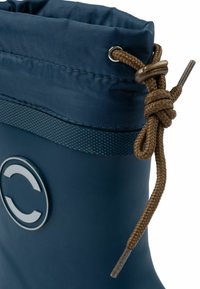 Botte en caoutchouc bleue avec une semelle texturée, un poignet élastique et un cordon tressé marron, présentant un logo circulaire sur le côté.