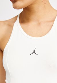 Bijela majica bez rukava izrađena od glatkog materijala, koja ima crni Jumpman logo na prsima, okrugli izrez i prilagođeni dizajn.