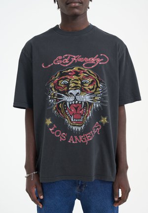 Camiseta negra de gran tamaño con un gráfico de tigre colorido adornado con rhinestones y el texto "Ed Hardy Los Ángeles". Material de algodón con mangas cortas.