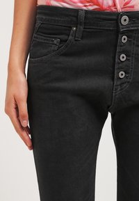 Svarta jeans i denim med hög midja, med knappgylf, fem fickor och sömnadsdetaljer längs sömmarna. Slät struktur.
