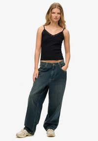 Top de tirantes de encaje negro combinado con pantalones de mezclilla sueltos de un azul intermedio y zapatillas crema. Textura casual y suave con un ajuste relajado.