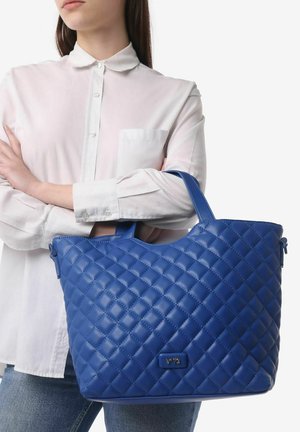 Sac fourre-tout matelassé bleu en matériau synthétique, avec un dessus arrondi et des poignées doubles. Le sac présente un accent logo subtil à l'avant.
