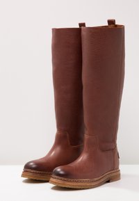 Bruna läderknästövlar med strukturerad yta, rund tå och kontrasterande sula. Har subtila sömmar och bakre dragremmar.