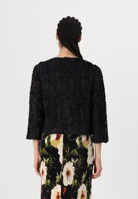 Black jacket with three-quarter sleeves, featuring textured floral appliqué. The outfit is paired with a floral patterned skirt.