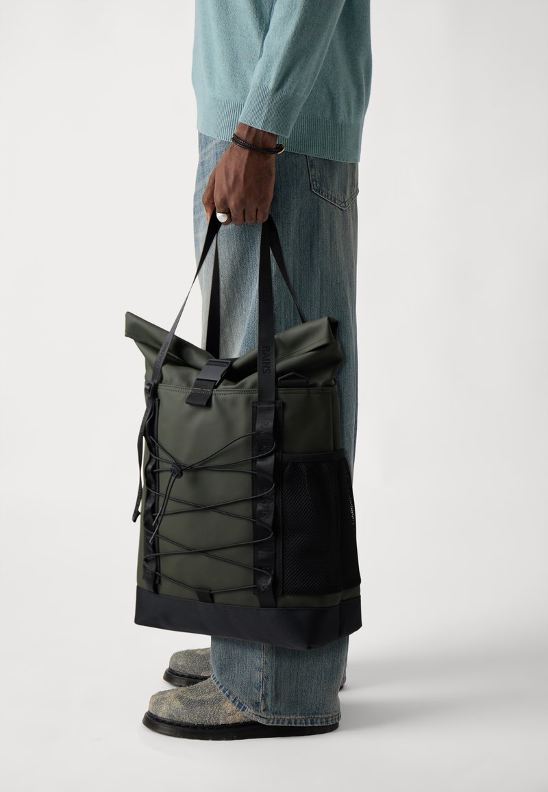 Grüner wasserdichter Tragetasche mit einem Roll-Top-Design, verstellbaren Trägern und einer seitlichen Netzertasche, mit schwarzen Akzenten und einer eleganten, glatten Textur.